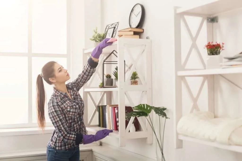 woman dusting top of bookshelf 