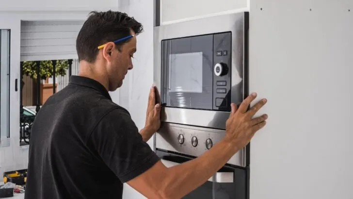 Man fitting a microwave in the hole of newly built kitchen
