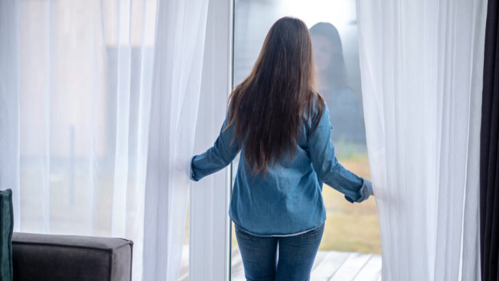 Woman standing at the glass door with white curtain